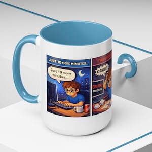 May include: A white ceramic mug with a blue interior, handle, and accent. The mug features a comic strip design with text that reads "JUST 10 MORE MINUTES..." and "FRUSTRATED! ERROR! CODE BUG!" The design depicts a person working on a computer.