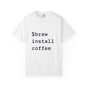 May include: White t-shirt featuring the text "$brew install coffee" in dark blue. The shirt has a crew neck and short sleeves. The text is centrally positioned on the front of the garment.
