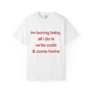 Op de afbeelding: Wit T-shirt met de rode tekst "im boring baby, all i do is write code & come home". Het shirt heeft een ronde hals en korte mouwen. De stof lijkt een zachte katoenmix te zijn.