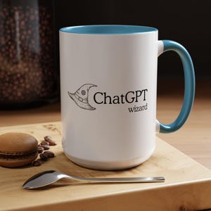 Peut inclure: Mug en céramique blanche avec intérieur et anse bleus. Le mug présente un dessin au trait noir d'un chapeau de sorcier et les mots "ChatGPT wizard" en noir. Une cuillère et un macaron sont sur une surface en bois.