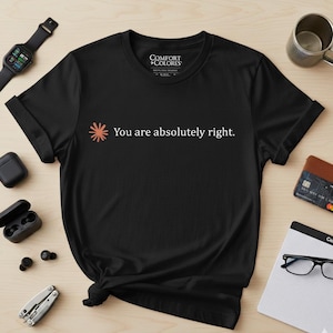 May include: Black t-shirt with the text "You are absolutely right." in white. The shirt features a small orange and white graphic. The shirt is made of a soft material and is suitable for casual wear.