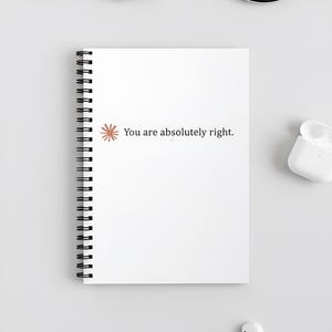 Może przedstawiać: Biały notatnik w spiralnej oprawie z napisem "You are absolutely right." czcionką szeryfową. Mała, pomarańczowa grafika kwiatowa znajduje się po lewej stronie tekstu. Notatnik leży na białej powierzchni.