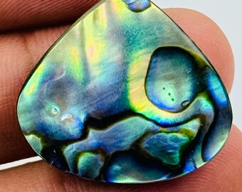 Puede incluir: Un cabujón de concha de abulón en forma de lágrima con una superficie pulida e iridiscente, que presenta patrones arremolinados de tonos azul profundo, verde vibrante y amarillo brillante que cambian según el reflejo de la luz.