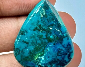 以下が含まれることがあります： ティアドロップ型のカボションカットの宝石。表面は研磨されており、ターコイズ、深い青、濃い緑のまだら模様が鮮やかに混ざり合っています。石は滑らかで光沢のある仕上がりで、上部が尖った洋梨のようなシルエットをしています。