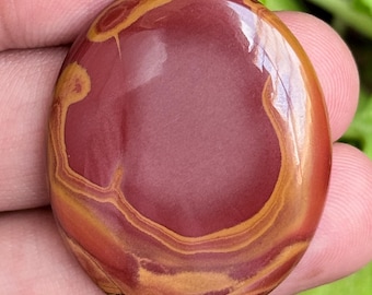 Puede incluir: Una piedra preciosa pulida de forma ovalada con una superficie lisa y patrones en espiral de colores rojo intenso, naranja quemado y amarillo dorado. La piedra tiene un acabado brillante y muestra bandas naturales en su estructura plana.