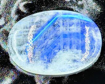 以下が含まれることがあります： 半透明の乳白色のベースに、表面全体に鮮やかで際立った青いシラー（アデュラレッセンス）が輝く、楕円形のムーンストーンのカボション。宝石には内部インクルージョンが見られ、表面は滑らかに磨かれたドーム状になっています。