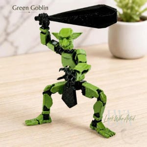 May include: A Green Goblin figurine featuring a bright green articulated body with black joints and a black loincloth. The figure is posed in a dynamic stance, holding a large, solid black club-like weapon raised above its head.