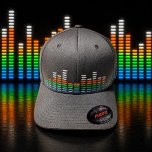 May include: A dark gray baseball cap featuring an embroidered graphic of a colorful audio equalizer spectrum across the front panels. The cap includes a circular black sticker on the brim with the text Flexfit The Original XL/XXL It Fits Your Life.