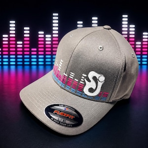 May include: A grey baseball cap featuring an embroidered white letter S logo and a horizontal graphic of pink and blue sound wave bars. The brim displays a black oval sticker with the text Flexfit The Original L/XL It Fits Your Life.