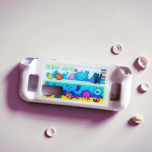 May include: A white plastic game console case with an "Ocean World" design. The design features cartoon sea creatures like whales, jellyfish, and fish. Several white buttons are scattered around the case.