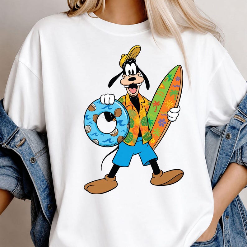 May include: A white t-shirt featuring a graphic of the cartoon character Goofy wearing a yellow cap, an orange floral shirt, and blue shorts. Goofy is holding a blue coconut-patterned swim ring in one hand and a colorful surfboard in the other.