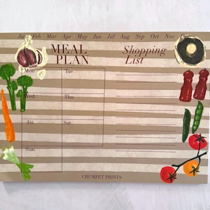 May include: A rectangular meal planner notepad with horizontal beige and white stripes. It features a weekly grid labeled Mon through Sun, a shopping list section, and illustrations of garlic, broccoli, carrots, mushrooms, peppers, peas, and tomatoes.