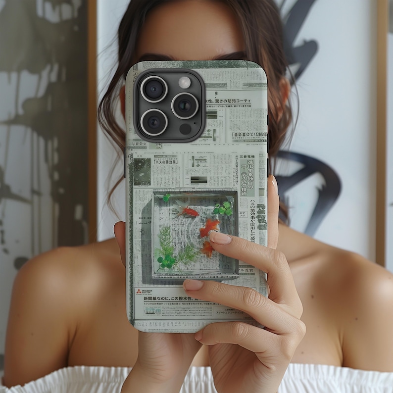 May include: A smartphone case with a unique design featuring a small aquarium with goldfish and aquatic plants. The case has a newspaper print background. The phone case has a triple-lens camera.