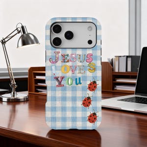 May include: A phone case with a blue and white gingham pattern. The words "JESUS LOVES YOU" are displayed in colorful, floral-patterned letters. Three red ladybugs with black spots are also featured on the case.