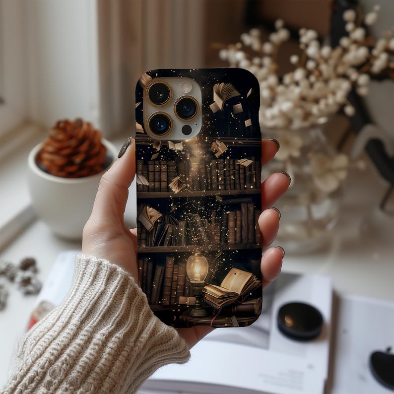 May include: A phone case featuring a detailed illustration of a library with books on shelves, a glowing lamp, and floating books. The design has a dark background with golden light effects, creating a magical and whimsical aesthetic.