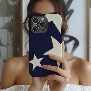 May include: A navy blue and cream-coloured phone case with a star design. The case has a dark blue background with two large cream-coloured stars. The phone case is held in front of a person.