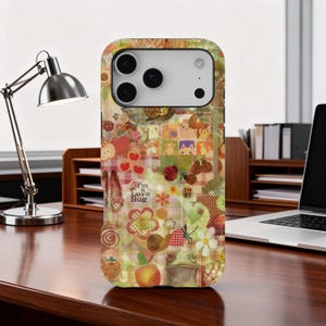 Op de afbeelding: Kleurrijke telefoonhoes met een collage-ontwerp. De hoes heeft illustraties van bloemen, fruit, slakken en de tekst "I'm a Love Bug". De hoes ligt op een houten bureau.
