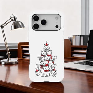 May include: A white phone case featuring a whimsical illustration of a Christmas tree made of cats. The cats are in various poses, wearing festive hats and scarves in red and white. The case has a glossy finish.