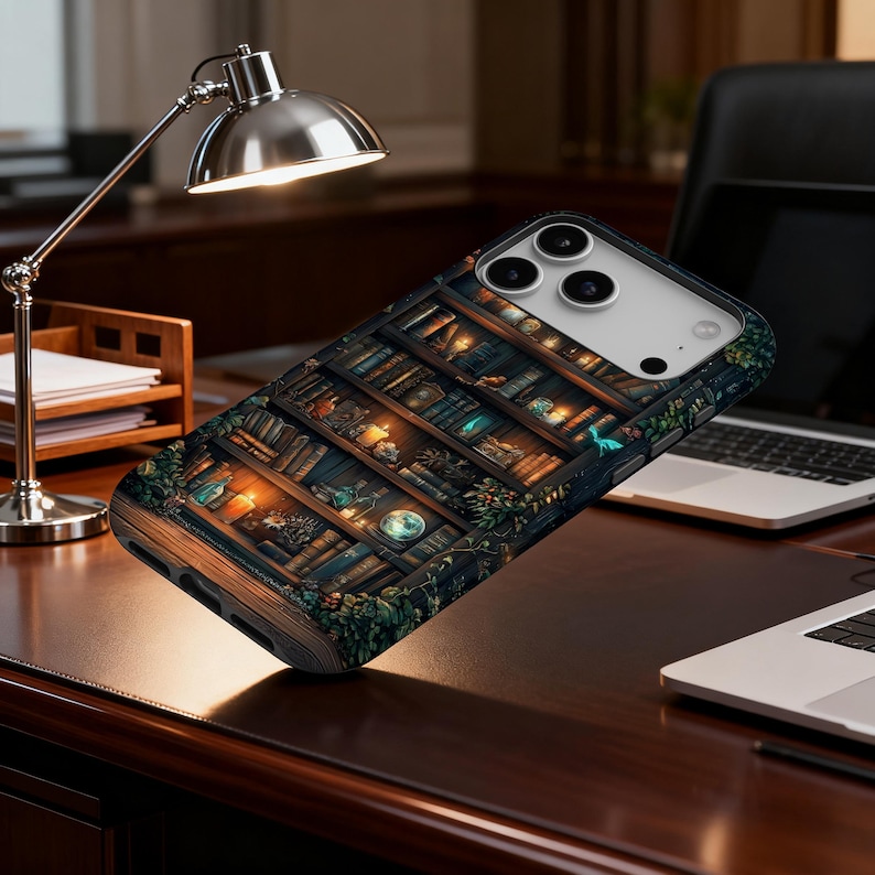 May include: A phone case featuring a detailed illustration of a bookshelf filled with books, candles, and decorative items. The case has a dark, vintage aesthetic with warm lighting and a touch of fantasy. The case is shown on a wooden desk.