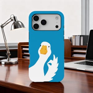 May include: A blue phone case with a white goose illustration giving the 'okay' hand gesture. The goose has an orange beak and is set against a blue background. The case is on a wooden desk.