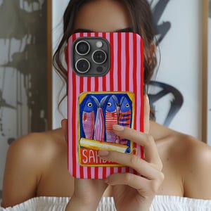 Puede incluir: Funda de teléfono con rayas rojas y rosas. La funda presenta una imagen rectangular de sardinas enlatadas, con la palabra "Sardines" visible. Las sardinas están representadas con detalles azules, rosas y rojos.