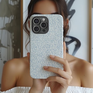 May include: A phone case with a white background and blue script text. The case has a camera cutout and is held in front of a person's face. The text appears to be in a foreign language.