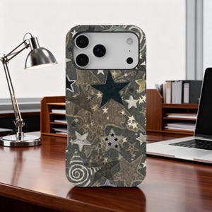 Puede incluir: Una funda de teléfono con un patrón de estrellas en tonos grises, dorados y negros. La funda presenta una variedad de formas de estrellas, incluyendo estrellas de cinco puntas y cúmulos de estrellas. El diseño tiene una apariencia texturizada.