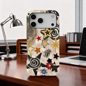 Puede incluir: Funda de teléfono decorativa con un fondo nacarado y un collage de estrellas doradas, rojas y negras. El diseño incluye una bola de discoteca y un gráfico de planeta. Un accesorio elegante.