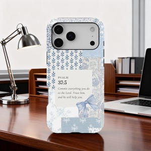 May include: A light blue and white phone case with a floral and leaf pattern. The case features the text "PSALM 37:5" and a quote about trusting in the Lord. The case is on a wooden desk.