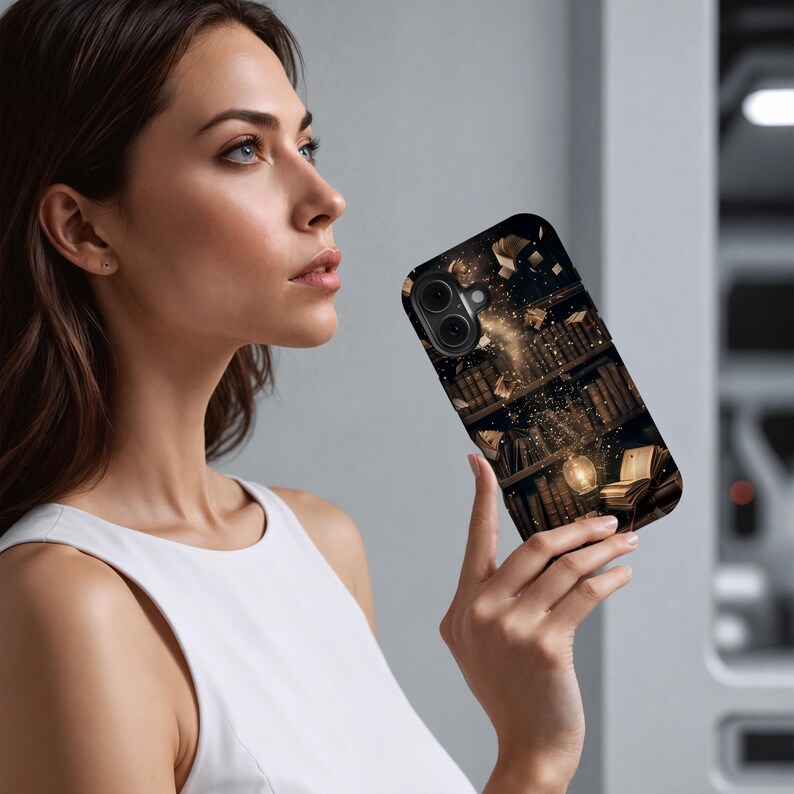 May include: A black phone case featuring a detailed illustration of a library with books, a glowing orb, and floating books. The design has a warm, inviting color palette with shades of brown and gold. The case is held by a person.