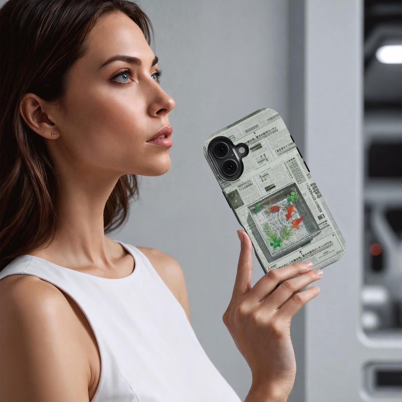 May include: A smartphone case featuring a newspaper print design. The case has a rectangular window with a koi fish illustration in shades of red, orange, and green. The case is held by a person.