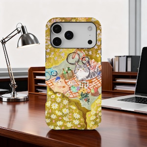 May include: A phone case featuring a whimsical picnic scene with two cats, a bicycle, and picnic basket. The case has a yellow floral background and a detailed illustration of the picnic setting.