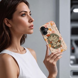 May include: A phone case with a floral pattern in peach, orange, and green. The case features the text "The Lord will fight for you, you need only be still" in a stylized font. The case is held by a person.