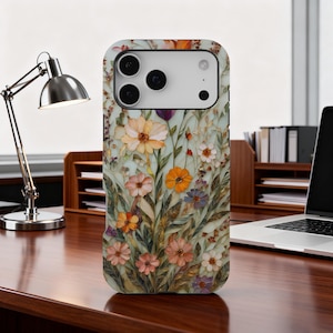 Pode incluir: Capa de telefone com design floral. A capa apresenta uma variedade de flores em tons de laranja, rosa, roxo e branco sobre um fundo verde claro. A capa tem um acabamento brilhante e um recorte para a câmera.