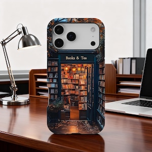 May include: A phone case featuring a detailed illustration of a bookstore entrance with the text "Books & Tea" above the door. The case has a dark blue frame and a warm, inviting interior scene with bookshelves and soft lighting.