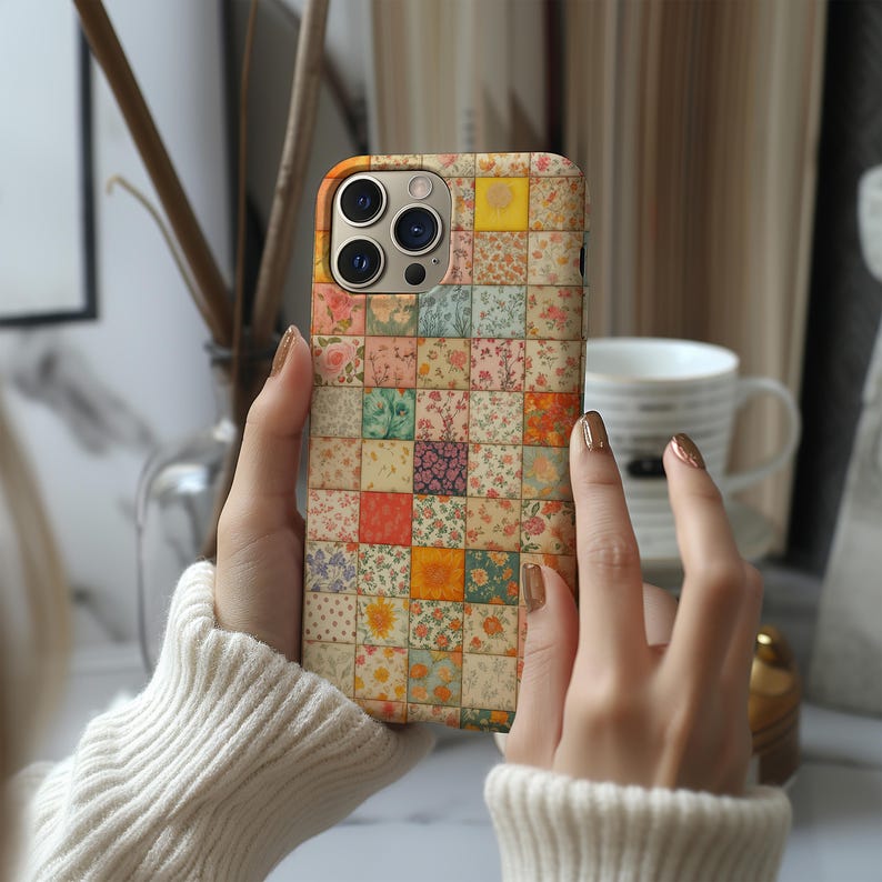 May include: A floral patchwork design phone case. The case features a grid of small squares, each with a different floral pattern in shades of pink, yellow, orange, and green. The case is held in front of a blurred background.