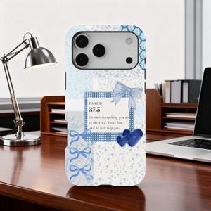 Puede incluir: Funda de teléfono floral azul claro y blanco con un versículo bíblico del Salmo 37:5. La funda presenta lazos y corazones azules. La funda del teléfono está sobre un escritorio de madera.
