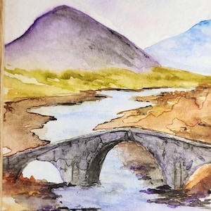 Könnte beinhalten: Aquarellmalerei einer Steinbrücke über einem Fluss, mit Bergen im Hintergrund. Das Kunstwerk ist in einem hellbraunen Holzrahmen gerahmt. Das Gemälde zeigt Farbtöne von Lila, Blau, Gelb und Braun.