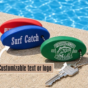 May include: Three oval-shaped foam floating keychains in red, blue, and green. The blue keychain features the white text Surf Catch. The green keychain displays a white Fishing Club logo with a fish graphic. A metal key is attached to the green keychain.
