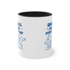Pode incluir: Caneca de cerâmica branca com borda interior preta. A caneca apresenta ilustrações de desenhos animados azuis e o texto "SMALL steps EVERY DAY". O design inclui uma flor e uma tartaruga.