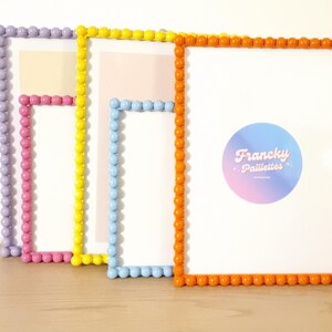 May include: A collection of colorful picture frames with beaded edges. The frames are in shades of purple, pink, yellow, blue, and orange. The orange frame has a circular logo with the text "Francky Paillettes".