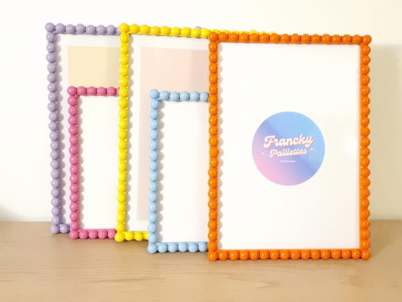 May include: A collection of colorful picture frames with beaded edges. The frames are in shades of purple, pink, yellow, blue, and orange. The orange frame has a circular logo with the text "Francky Paillettes".