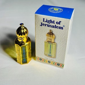Pode incluir: Um frasco de perfume dourado com uma tampa decorativa em forma de coroa e uma caixa a condizer. A caixa e o frasco apresentam o texto "Light of Jerusalem". O frasco tem 12 ml.