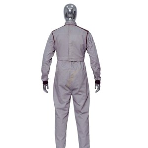 May include: A gray jumpsuit with long sleeves and a matching pant leg design. The jumpsuit has dark brown trim along the shoulders, collar, and cuffs. The mannequin is wearing the jumpsuit, and the back of the jumpsuit is visible.