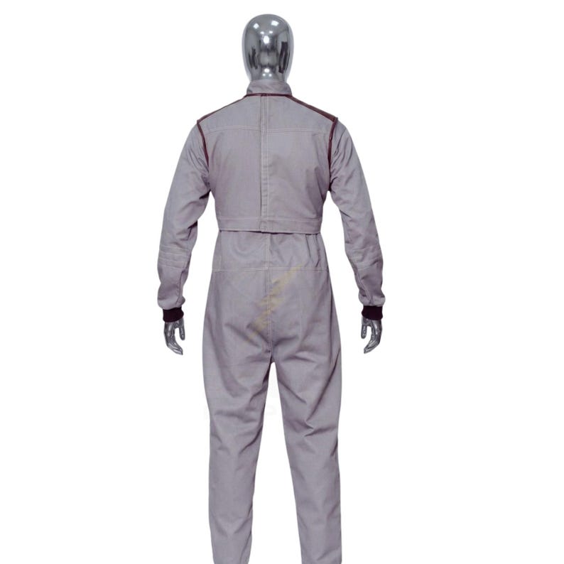 May include: A gray jumpsuit with long sleeves and a matching pant leg design. The jumpsuit has dark brown trim along the shoulders, collar, and cuffs. The mannequin is wearing the jumpsuit, and the back of the jumpsuit is visible.