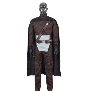 May include: A brown costume with a black cape, gloves, and a utility belt. The costume includes a brown jumpsuit, a white midsection, and a brown shoulder strap. The mannequin has a silver head.