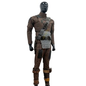 May include: A brown tactical costume set displayed on a black mannequin. The outfit includes a long-sleeved shirt, trousers with dark patches, a utility belt with a grey chest plate, a shoulder strap with ammunition loops, and leg wraps with buckles.