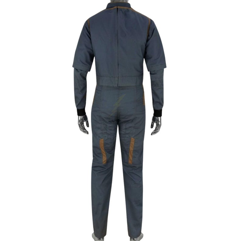 May include: A gray jumpsuit with brown accents. The jumpsuit has long sleeves with black cuffs, a collar, and a zipper down the front. Brown stitching and patches are visible on the garment. The jumpsuit is displayed on a mannequin.