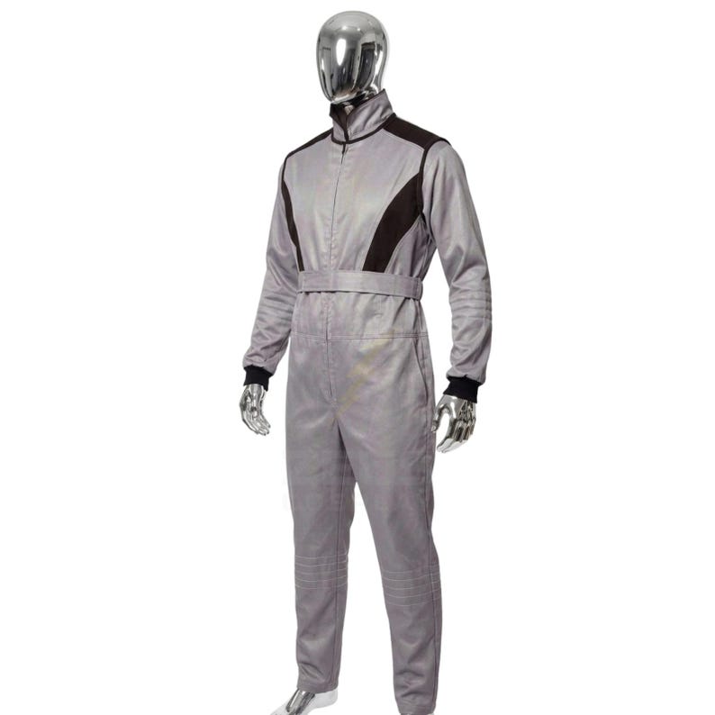 May include: A gray racing suit with black accents on the shoulders and upper chest. The suit has a zip-up front, a belt at the waist, and black cuffs at the wrists and ankles. The suit is displayed on a mannequin.