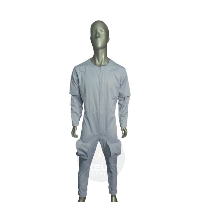 以下が含まれることがあります： 長袖と太ももに大きなポケットが付いた、明るいグレーのジャンプスーツ。マネキンに着せられています。この衣装はシンプルで実用的なデザインです。